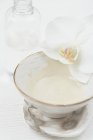 Vista close-up de leite em uma tigela pequena com uma flor branca e garrafa de vidro — Fotografia de Stock