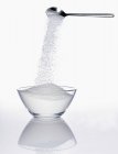 Сахар течет из ложки в миску — стоковое фото
