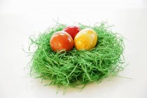 Vista de primer plano del nido de Pascua con tres huevos de colores - foto de stock