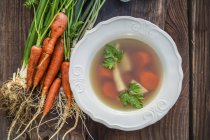 Homemade fresh vegetable broth on white plate over wooden surface — Stock Photo