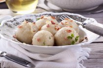 Potato dumplings with bacon on white plate over towel — Stock Photo