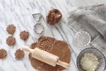 Top view of gluten-free pastry rolled out with a rolling pin by cutters and a bowl of flour on a marble surface — Stock Photo