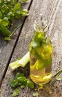 Una bevanda disintossicante con sedano ed erbe in bottiglia sulla superficie di legno — Foto stock
