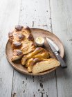 Un pain de levure tressé, du beurre et un couteau sur une assiette en bois — Photo de stock