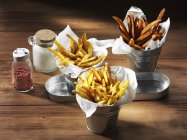 Three types of chips with a salt shaker and pink pepper on a rustic wooden surface — Stock Photo