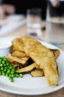 Pesce e patatine fritte con piselli su piatto bianco — Foto stock