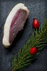 Closeup view of slice of smoked, marinated duck breast with a sprig of spruce and rose hips on a slate platter — Stock Photo