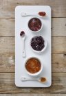 Vista superior de tres tipos de mermelada en cuencos con cucharas en una tabla - foto de stock