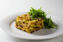 Pièce de lasagne avec salade de roquette — Photo de stock