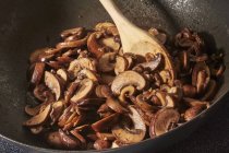 Brown mushrooms being fried with chopped garlic in olive oil in a wok — Stock Photo