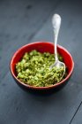 Closeup view of wild garlic Pesto with a spoon in a red bowl on a wooden surface — Stock Photo