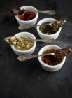 Vista de cerca de cuatro tipos de té en cucharas vintage sobre cuencos - foto de stock