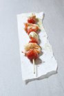 A prawn and tomato skewer on paper over grey surface — Stock Photo