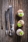 Three snails with garlic butter and parsley on wooden surface by fork and tongs — Stock Photo