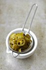 Pickled jalapeos in a sieve over stone surface — Stock Photo