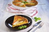 Chicory and carrot tart on black plate  over wooden surface with fork and knife — Stock Photo