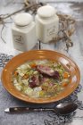 Зимнее овощное рагу с огурцами и беконом на коричневой тарелке за столом — стоковое фото
