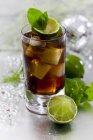 Closeup view of Cuba Libre cocktail with lime, ice cubes and leaves — Stock Photo