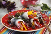 Marinated herring with peppers and olives on red plate with fork — Stock Photo