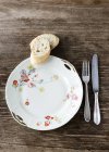Top view of an old white porcelain plate decorated with flowers with silver cutlery and two slices of baguette on the wooden table — Stock Photo