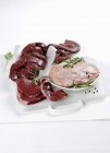 Closeup view of veal innards with sage and rosemary on a white chopping board — Stock Photo