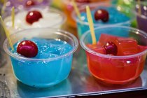 Vista de cerca de gelatinas de colores con cerezas en cuencos de plástico - foto de stock
