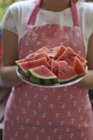 Eine Frau mit Schürze hält einen Teller mit Melonenscheiben, Mittelteil — Stockfoto