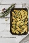 Rosemary potatoes ready to roast in dish on wooden surface — Stock Photo
