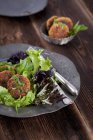Quinoa fritters on a bed of lettuce on grey plate over wooden surface — Stock Photo