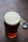Vidro de cerveja âmbar com um abridor de garrafas — Fotografia de Stock