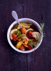 Жареные овощи с розмарином в миске с ложкой на деревянной поверхности — стоковое фото