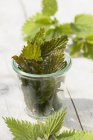 Смажене листя кропиви в скляному горщику над дерев'яною поверхнею — стокове фото