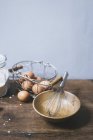 Closeup view of an arrangement of eggs in a wire basket and a wooden bowl with a whisk — Stock Photo