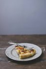 A slice of tomato quiche on plate on wooden surface over grey background — Stock Photo