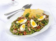 Piselli con tonno e uova - горох з тунцем та яйцем на білій тарілці — стокове фото