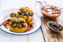 Gelbe Paprika gefüllt mit Oliven auf weißem Teller über Holzoberfläche — Stockfoto