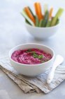Beetroot hummus in white bowl over towel with knife — Stock Photo