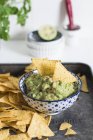 Bowl of Guacamole with Chips over black tray — Stock Photo