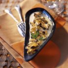 Mussels with cream in small black dish over towel with fork and knife — Stock Photo