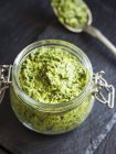 Pesto vegano a base de hierbas mezcladas en un frasco abierto y en una cuchara - foto de stock