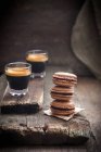 Closeup view of piled macarons with glasses of coffee on paper and wooden boards — Stock Photo