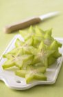 Нарезанные звездные фрукты на белом столе над зеленой поверхностью ножом — стоковое фото