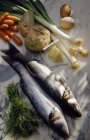 Bass fish laying on white surface with vegetables — Stock Photo