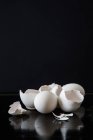 Vista de cerca de huevos blancos y cáscaras en la superficie reflectante negro - foto de stock