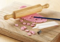 Primo piano vista di glassa rosa stesa su una tavola con mattarello, taglierina a forma di fiore in metallo e tubo di glassa bianca — Foto stock