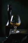Vista ravvicinata di bottiglia e bicchiere di mela francese Calvados sulla tovaglia nera — Foto stock