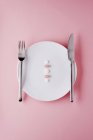 Top view of medicine pills with knife and fork on white plate and pink surface — Stock Photo