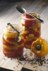 Jars of yellow and red peppers with spoons over wooden surface — Stock Photo