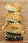 Small spinch pies on straw mat over wooden surface — Stock Photo