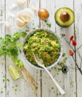 Guacamole with ingredients on rustic wooden surface — Stock Photo